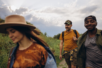 Group of friends, young men and women walking, strolling together outskirts of city, in summer forest, meadow. Active lifestyle, friendship, care, ecology concept
