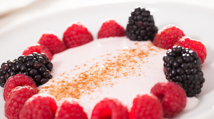 raspberries and blackberries laid out on a white plate in circle with yogurt and cinnamon
