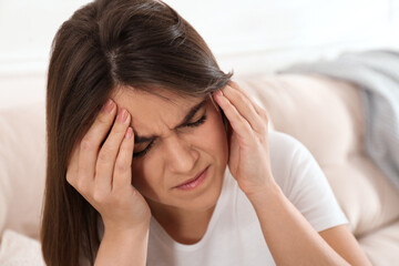 Young woman suffering from migraine on sofa at home