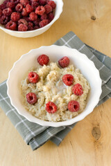 Milk barley porridge with butter and raspberries in white bowl on wooden background