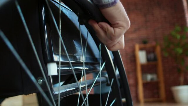 Closeup male hand turning wheels of wheelchair. Rolling wheelchair with disabled man, back view. Macro. Concept of diagnosis and disability