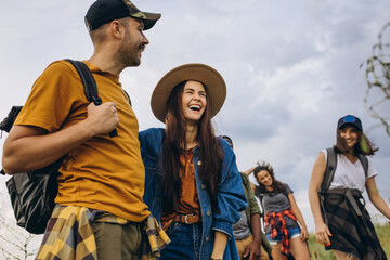 Group of friends, young men and women walking, strolling together in summer forest, meadow. Active lifestyle, friendship, care, ecology concept