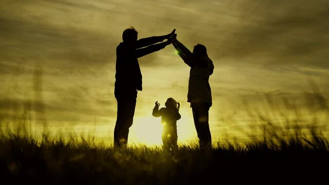Silhouette of happy family, playing with little daughter, symbol of family at home in sun. Mom, Dad, with their hands they depict roof of house over head of child. I dream of joint home. House builder