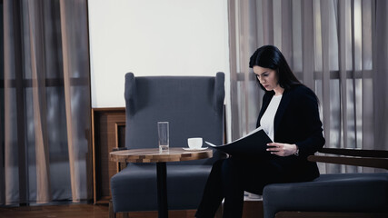 Businesswoman looking at paper folder with documents in lobby of restaurant