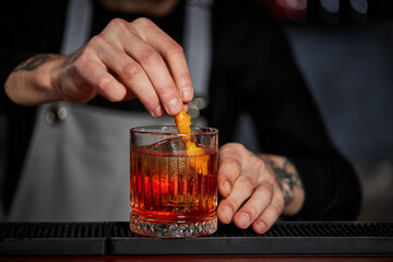 bartender makes a cocktail in a glass with orange peel
