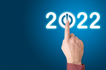 hand presses the start button for 2022. Finger about to press button with the text 2022 start. Year two thousand and twenty two concept. copy space. blue background