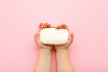 Baby girl hands holding white natural soap on light pink table background. Pastel color. Closeup....