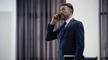 Businessman with paper folder talking on cellphone in lobby of restaurant