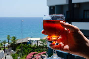 Caucasian man holding glass of drink with condensate. Close-up glass of cold wine on blurred background of building, blue sky and turquoise sea with copy space. Sea vacation concept.