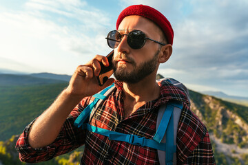 A male traveler in a red hat with a backpack is talking on the phone against the background of...
