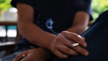 Closeup man cigarette burning smoke in hand. Tobacco smoke spreads carcinogens and the COVID-19...