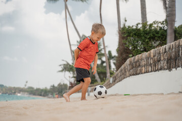 Boy playing barefoot soccer on the beach with a black and white ball on an island by the sea