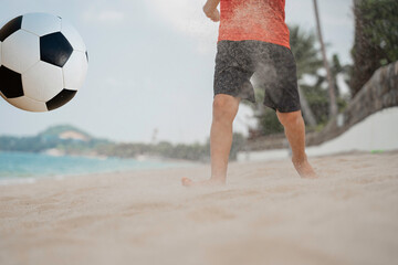 Boy playing barefoot soccer on the beach with a black and white ball on an island by the sea