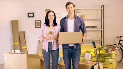 Fototapeta na wymiar Cheerful couple with box and plant in new home