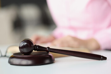 Judge wooden gavel lying on table against background of woman with book closeup