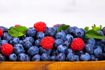 Blueberry and Raspberry With a Green Mint leaf in a Wooden Bowl on a white top view, Summer Freshly Berry, Copyspace