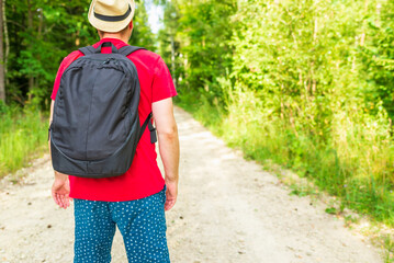 Back view of young man with backpack traveling alone forest on warm summer day.Tourism and active lifestyle concept.