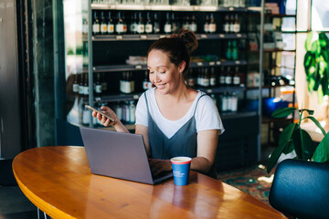 Satisfied happy relaxed woman has enjoyment using social media while sitting in a restaurant with a laptop.