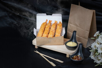 Shrimp tempura in paper packaging, dark background with smoke.