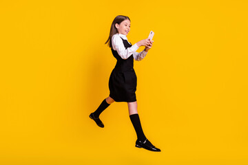 Fototapeta na wymiar Full length body size photo schoolgirl jumping browsing internet cellphone isolated vivid yellow color background