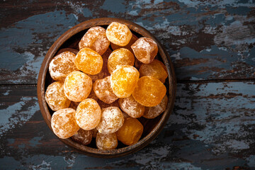 Candied citrus fruits with powdered sugar in a wooden bowl on a dark background. Candied kumquat.