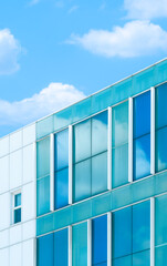 Low angle view of blue glass and white tile wall of modern office building against cloud and blue sky background in vertical frame 