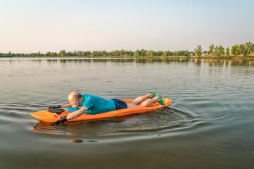 athletic, senior man is paddling a prone kayak on a lake in Colorado, this water sport combines aspects of kayaking and swimming