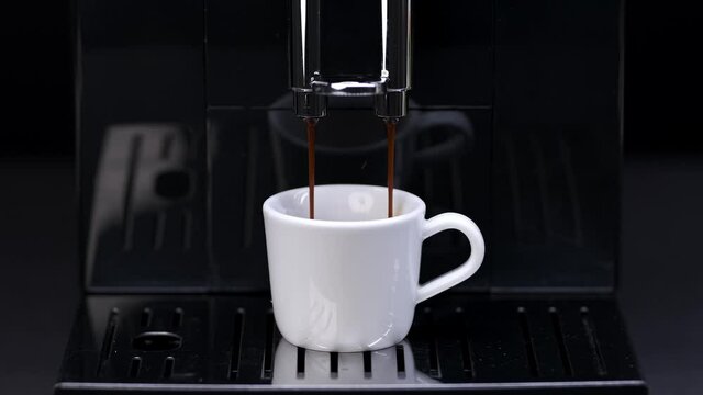 Automatic coffee machine pours espresso into a white cup
