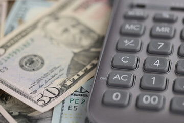 Gray calculator lying on dollar bills closeup