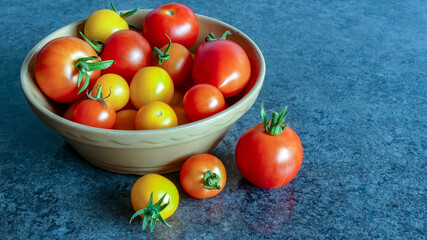 Landscape of freshly harvested organic mixed tomatoes. In a simple brown glazed bowl, sitting on blue grey marble. With others on surface. Selective focus, with space for text. Natural light. UK. - 450535618