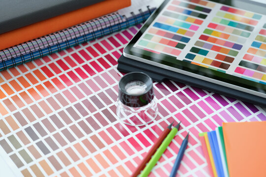 Magnifying glass lying on paper with color samples near digital tablet closeup