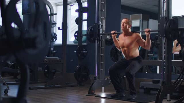 Senior fit man bodybuilder doing barbell squats at gym