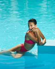 tanned slender girl in a pink swimsuit is resting in the pool under the rays of the sultry sun