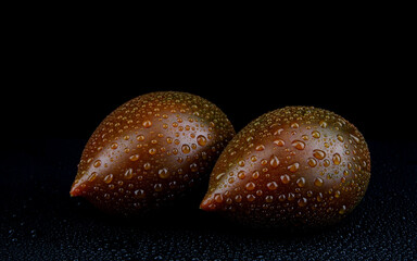 Two ripe cumato tomatoes with drops of water on the peel on a black background.