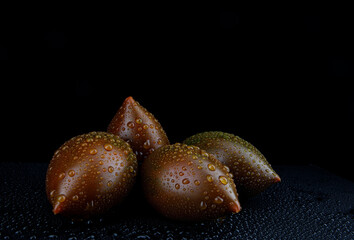Several ripe cumato tomatoes with drops of water on the peel on a black background.