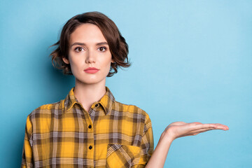 Photo of calm charming pretty girl palm hold empty space object wear plaid shirt isolated blue color background