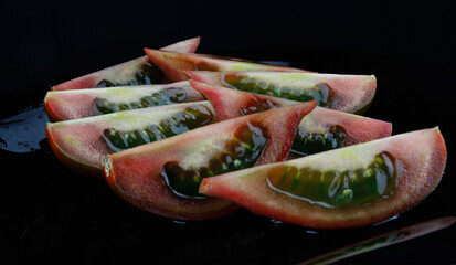 Sliced ripe cumato tomato on a black plate.