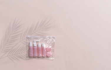Mock up feminine flatlay with small size cosmetic bottles in travelling bag on neutral pastel background. Palm leaves shadows. Minimal skin or body care products concept for vacation or journey.
