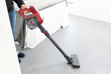 Woman working with a cordless vacuum cleaner in the modern bedroom of the house