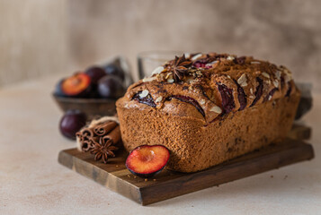 Homemade spicy plum cake decorated with almond on a wooden serving board, concrete background. Loaf cake with plum, spices and almond.