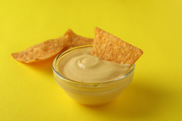 Bowl with cheese sauce and chips on yellow background