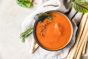 Tomato soup garnish with ground pepper, rosemary and bread sticks, light background.