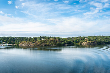 Fototapeta na wymiar Amazing panoramic view of beautiful evergreens small islands and rocky coast of Scandinavia on sunny summer day. Shot from cruise ship. Forest green long coastline. Water voyage to Sweden Stockholm.