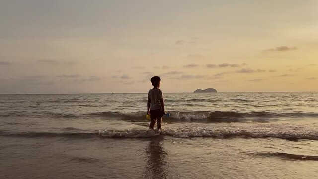 Silhouette view of a little Asian boy stands on the beach during a beautiful sunset, happy holiday and leisure outdoor activity.
