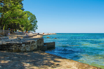 Tourists and locals enjoy the summer sun and sea on the coast just north of the historic centre of Porec on the Istria coast of Croatia
