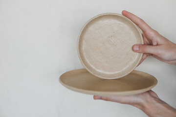 Hands holding ceramic plates isolated on white background. Minimalist set of handmade ceramic tableware and pottery