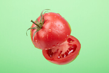Ripe tomato, cut in the air on a green background