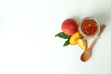 Jar of peach jam, ingredients and spoon on white background