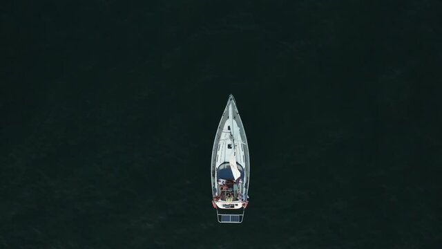 Cinematic shot of a drone from top to bottom on a sailing yacht drifting in the sea or ocean at sunset.