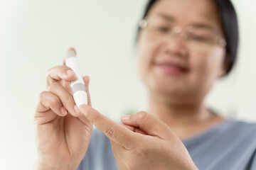 Mature Asian woman using lancet on finger for checking blood sugar level by Glucose meter,...